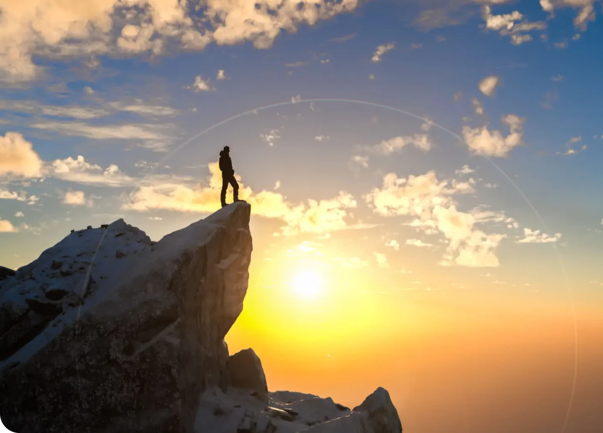 Person standing on mountain peak at sunrise.