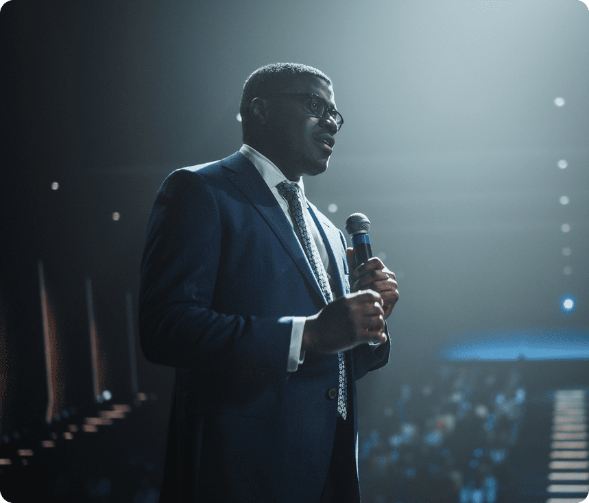 A man in a suit speaking on stage with a microphone.